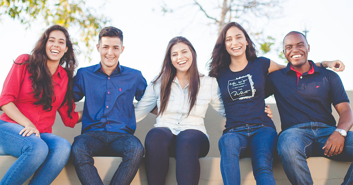 A group of students sat on a wall with their arms around each other